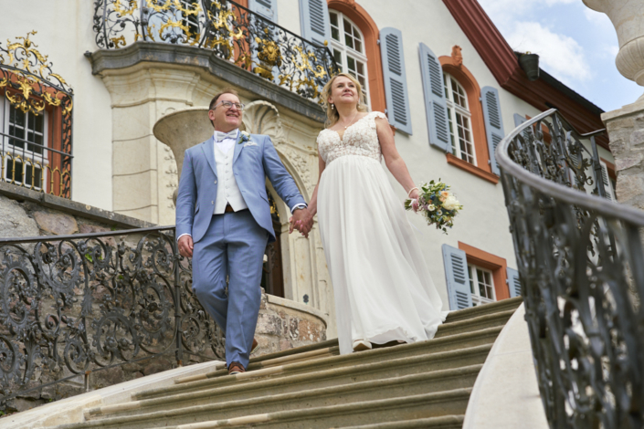 Brautpaar läuft Treppe herunter auf Schloss Bürgeln und der Hochzeitsfotograf wartet